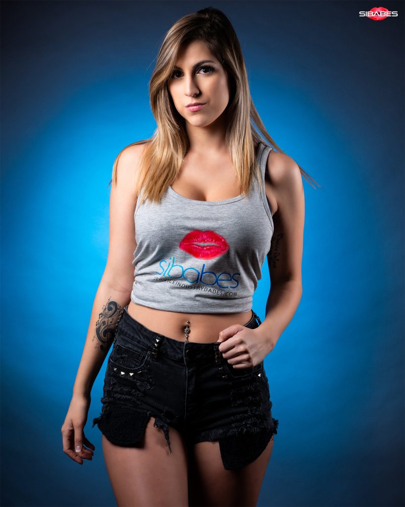 SIBABES studio portrait of a woman wearing a grey logo top against a blue backdrop.